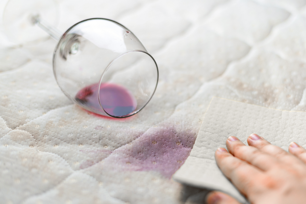 Ein umgefallenes Glas und ein Rotweinfleck auf einem Sofa